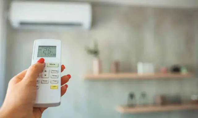 Mano con control remoto ajustando la temperatura ideal aire acondicionado para dormir a 25°C.