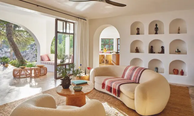 Comment habiller un mur blanc salon : des niches décorées d'objets ethniques et de poteries, un canapé incurvé, des fauteuils bouclette, et une vue sur un jardin luxuriant.