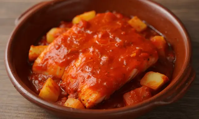 Bacalao a la riojana, un plato tradicional con trozos de patata y pimiento en una salsa roja sabrosa, servido en cazuela de barro.