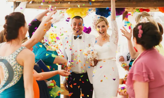 Glückliches Brautpaar im Konfettiregen, eine wunderschöne Tradition zur Hochzeit. Gäste werfen bunte Papierstreifen.