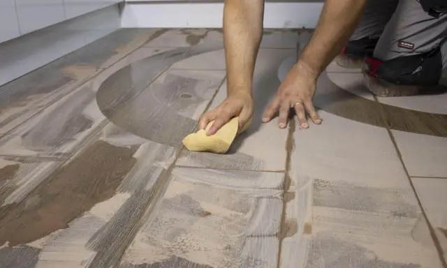 Man limpiando suelo porcelánico con una esponja. El suelo tiene un diseño de madera y un patrón curvo.