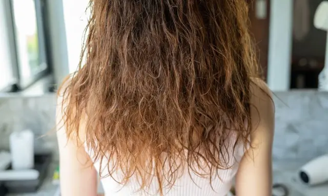 Wilgotne, brązowe włosy z widocznym **frizz** opadają na ramiona.