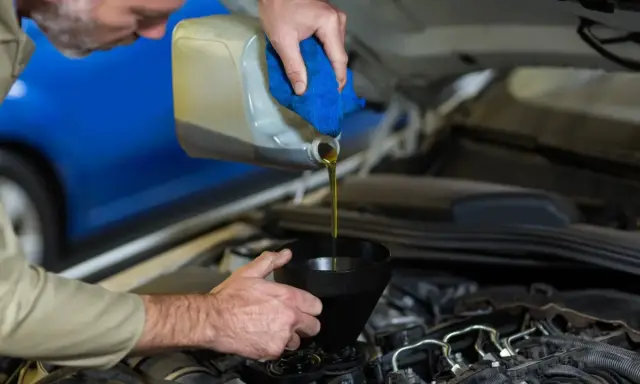 Mecánico vertiendo aceite nuevo en el motor para el mantenimiento del coche.