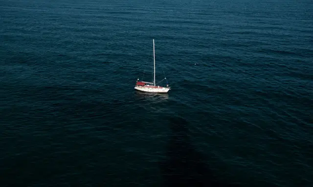 Un voilier blanc et rouge est au mouillage sur une mer sombre. La question est : combien de temps peut on rester au mouillage dans ce décor paisible ?
