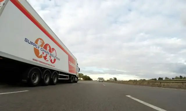 Camión de carga con el logo "Supply Chain Solutions" y "Turners" avanza por la autopista.