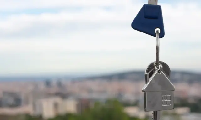 Llaves con un llavero en forma de casa, simbolizando un contrato de opción de compra. Fondo de ciudad difuminado.