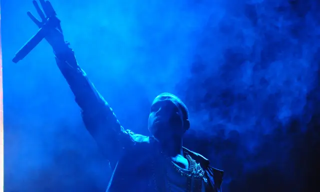 Kanye West z mikrofonem w dłoni, w niebieskiej poświacie. W tle dym, przypominający atmosferę z jego albumów.