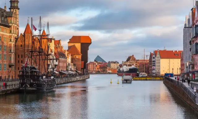 Gdańsk: zabytkowy żaglowiec cumuje przy Motławie, w tle Żuraw i nowoczesne budynki. Malowniczy opis miasta.