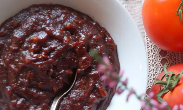 Gęsty, ciemny sos barbecue w białej misce, obok dojrzałe pomidory. Idealny przepis na domowy sos barbecue.