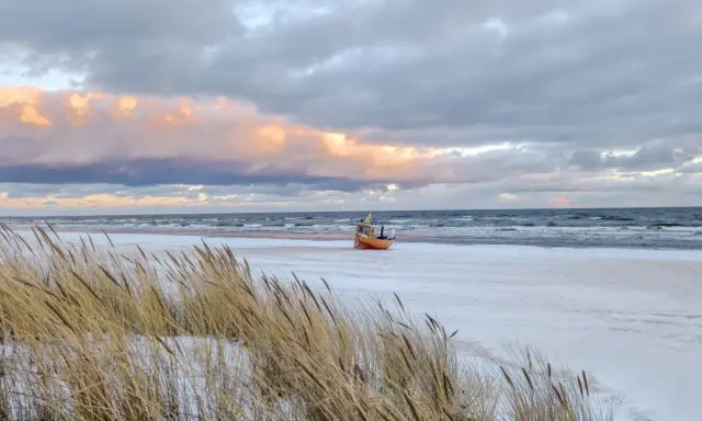 Ein kleines Boot liegt am verschneiten Strand der Ostsee, im Hintergrund die Seebrücke von Ahlbeck.