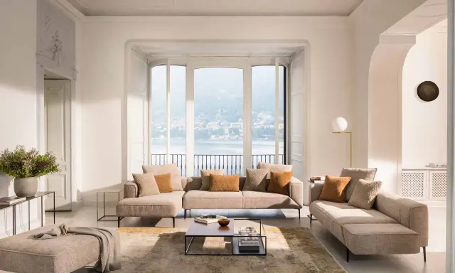 Un salon blanc et beige cocooning, avec des canapés confortables, un tapis doux et une vue imprenable sur un lac.