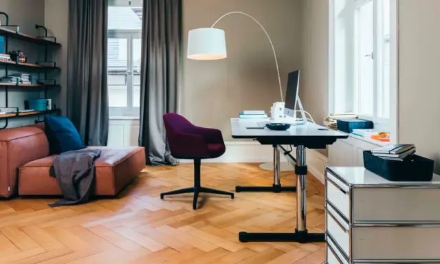 Accogliente stanza studio piccola con divano in pelle, scrivania regolabile, sedia viola e libreria a muro.