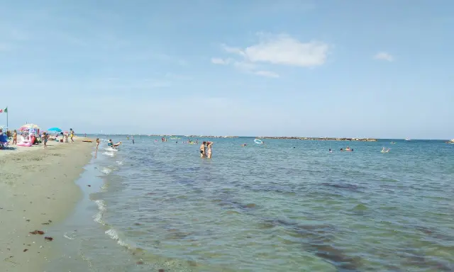 Gente che si gode il sole e il mare a Lido Adriano. Bambini giocano sulla sabbia, adulti nuotano e si rilassano nell'acqua cristallina.