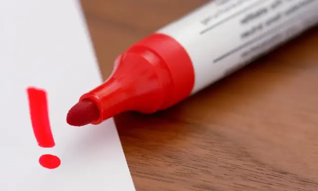 Roter Filzstift schreibt ein Ausrufezeichen auf weißes Papier. Ein wichtiger Hinweis, der sich leicht vom Filzstift von Haut entfernen lässt.
