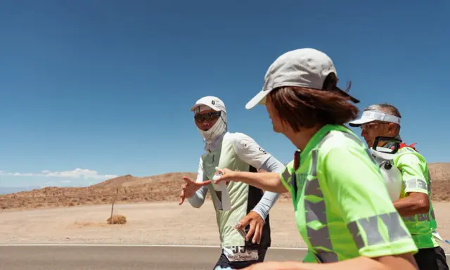 Läufer beim Badwater 135 Ultra-Marathon in der Wüste. Eine Helferin reicht einem Läufer Wasser.