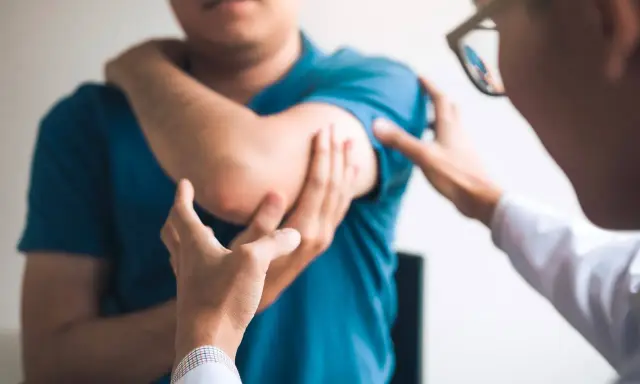 Un médecin examine le coude d'un patient, possiblement atteint du syndrome de la souris, une maladie professionnelle liée à l'usage intensif de l'ordinateur.