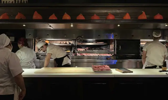 Chefs preparan cortes de carne en la parrilla Don Julio, con brasas ardientes y un ambiente de cocina profesional.