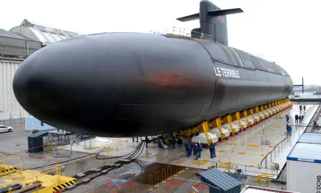 Le sous-marin "Le Terrible" est en cours de construction, sa taille impressionnante est mise en valeur sur des supports jaunes.