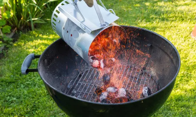 Encendiendo carbón con un chimenea para barbacoa. Chispas vuelan mientras se vierten las brasas calientes.