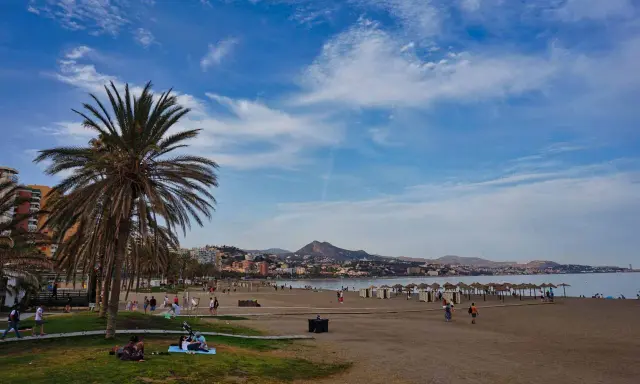Sonniger Strand an der Costa del Sol mit Palmen, Menschen und dem Meer im Hintergrund.