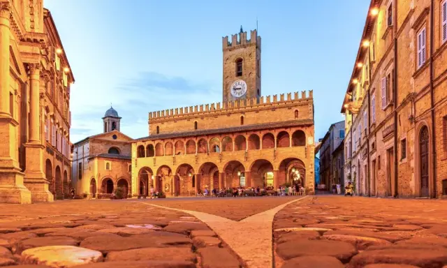 Piazza del Popolo a Ripatransone, un gioiello per un itinerario Marche 5 giorni. Edifici storici illuminati, torre con orologio e ciottoli antichi.