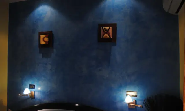 Pared azul con efecto veladura, dos cuadros abstractos y lámparas de pared.