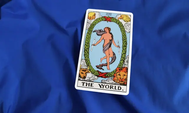 Karta "The World" z talii tarota, przedstawiająca nagą postać w tańcu, otoczoną wieńcem i symbolami czterech ewangelistów.