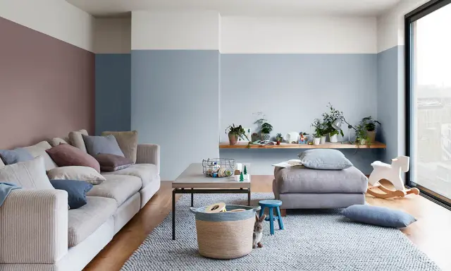 Soggiorno accogliente con divano beige, tappeto grigio e pareti color carta da zucchero. Un coniglietto curioso osserva dal cesto.