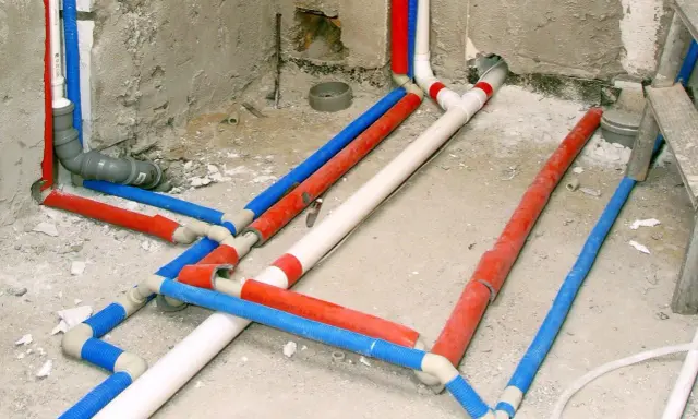 Skomplikowana instalacja wodociągowa z rurami w kolorach czerwonym, niebieskim i białym, przygotowana do ukrycia w ścianie.