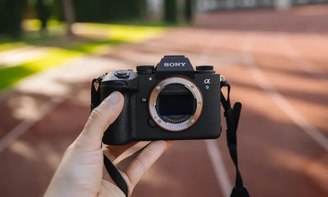 Dłoń trzyma aparat Sony Alpha 9 z obiektywem. Jego zaawansowany **global shutter** pozwala na uchwycenie dynamicznych scen bez zniekształceń.