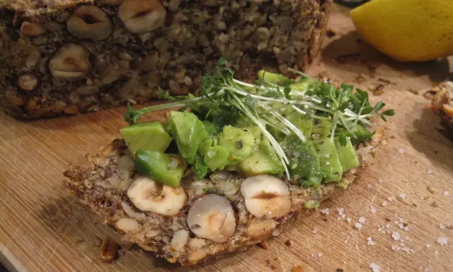 Ein Stück herzhaftes Flohsamenschalen Brot mit Nüssen, belegt mit Avocado und Kresse. Ein gesunder Genuss!