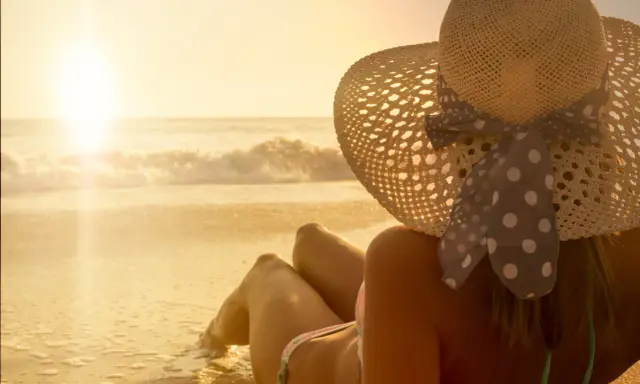 Donna con cappello di paglia e un bikini a pois, godendosi il tramonto sulla spiaggia. La sua pelle ha una perfetta abbronzatura arancione.