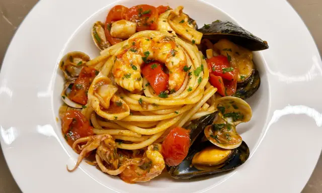 Spaghetti allo scoglio with shrimp, mussels, clams, squid, and cherry tomatoes in a white bowl.