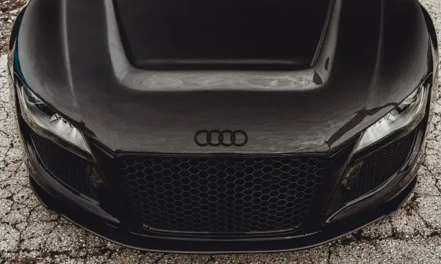 Przód czarnego Audi z maską z włókna węglowego. Widoczne reflektory, atrapa chłodnicy i logo marki.