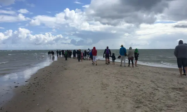 Folk promenerar längs en sandremsa vid vattnet norr om Skagen. Molnig himmel och hav.
