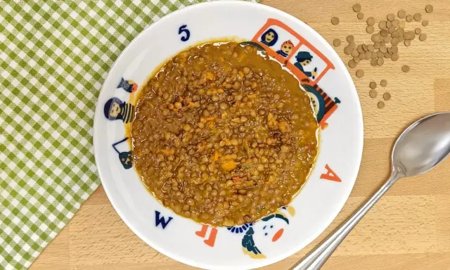 Un plato de lentejas bebé, cocinadas con zanahoria y especias, servido en un plato infantil con dibujos.