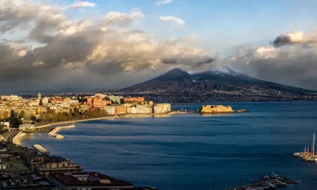 Vista panoramica di Napoli con il Vesuvio innevato sullo sfondo, il Castel dell'Ovo e il lungomare.