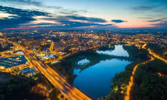 Widok z lotu ptaka na rozświetlone miasto nocą, z autostradą i trzema stawami w tle.