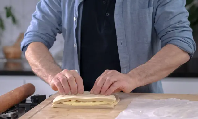 Un homme plie une pâte feuilletée professionnelle sur une planche en bois, prêt à créer des couches parfaites.