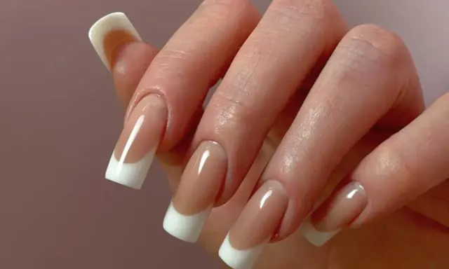 Dłoń z paznokciami w stylu odwrócony french. Klasyczny manicure z białym wykończeniem i naturalnym kolorem płytki.