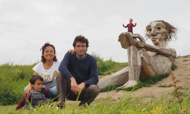 Familia disfrutando de Copenhague con niños, posando ante una escultura gigante de madera. Un niño pequeño juega en la mano de la figura.