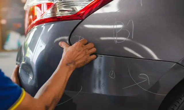 Ręce mechanika oceniają wgniecenia na karoserii samochodu, przygotowując się do usuwania uszkodzeń.