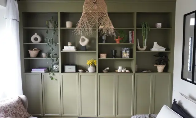Une belle idée de bibliothèque salon avec des étagères vertes remplies de vases, plantes, livres et objets déco.