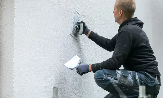 Man putsar en vit fasad med en bredspackel. Det är viktigt att man målar putsad fasad för att skydda den.