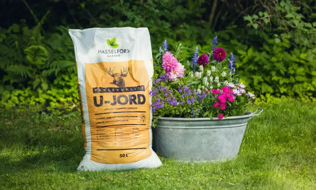 En säck Hasselfors U-jord bredvid en zinkbalja fylld med färgglada blommor i kruka.
