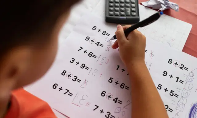 Dziecko zmagające się z zadaniami matematycznymi, być może z dyskalkulią. Widoczne są próby rozwiązywania przykładów i kalkulator.