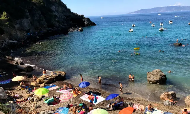 Spiaggia affollata con ombrelloni colorati e gente che nuota. Ecco come arrivare a Cala del Gesso per godersi questo mare cristallino.