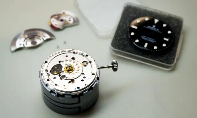 Parti di un movimento di orologio di lusso, tra cui il quadrante nero e la corona, pronti per l'assemblaggio.