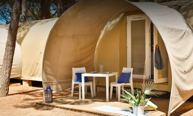 Tavolino e sedie con cuscini blu davanti a una tenda del **Gitavillage Il Gabbiano**. Lanterna blu e piante sul deck.