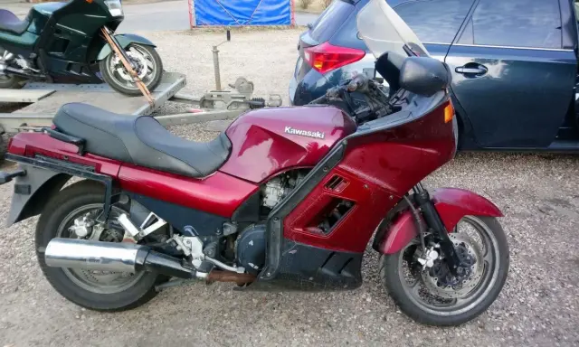 Czerwony motocykl Kawasaki GTR 1000 na przyczepce, obok ciemny samochód.